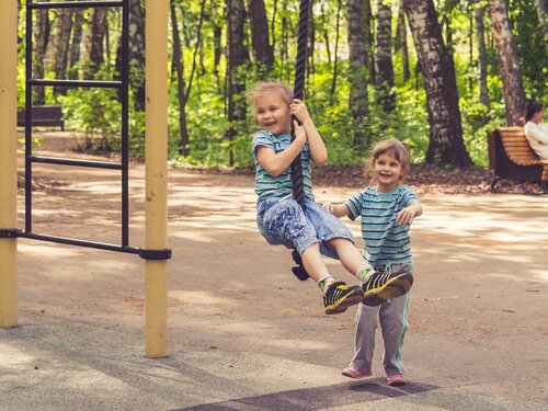 Photo of two young girls in a playground, with one swinging on a rope